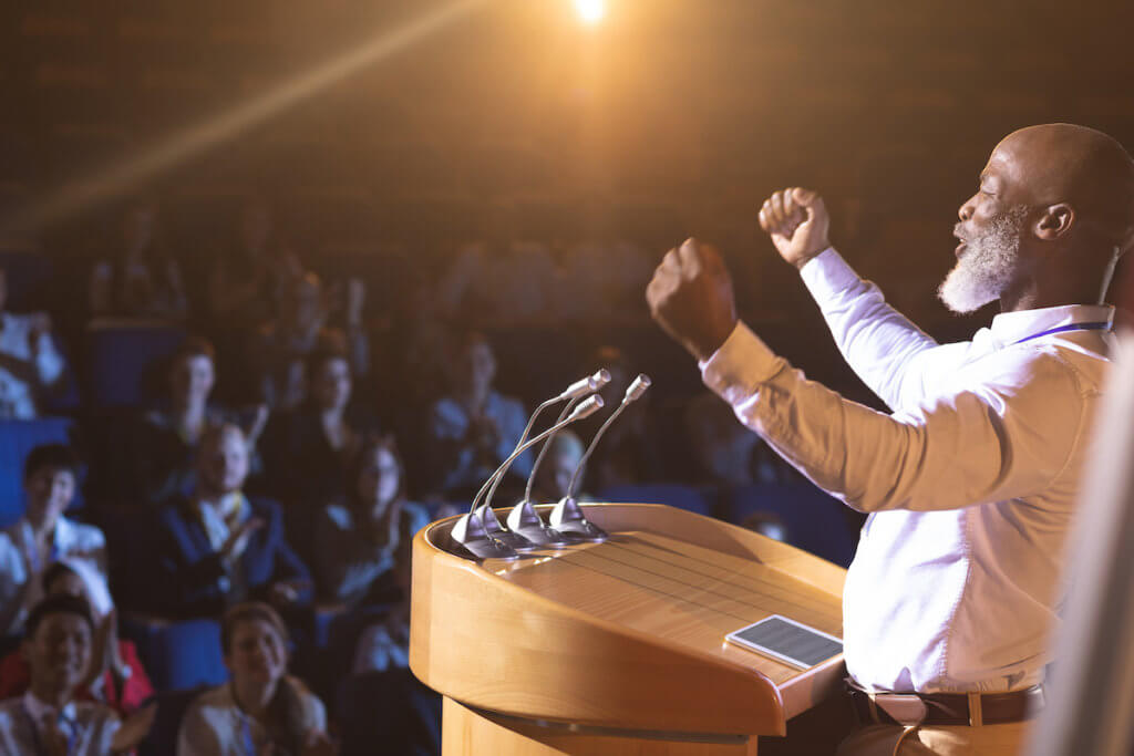 Man standing before a podium public speaking to an attentive audience